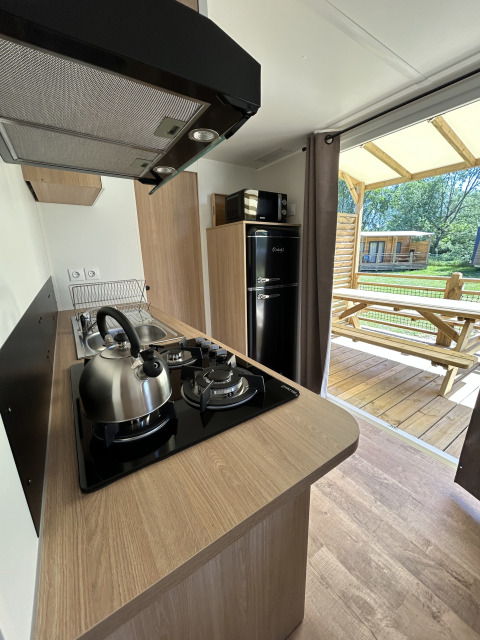 Cocina moderna en una cabaña de Camping Seasonova Les Marguerites, Francia, con vista a la terraza de madera.