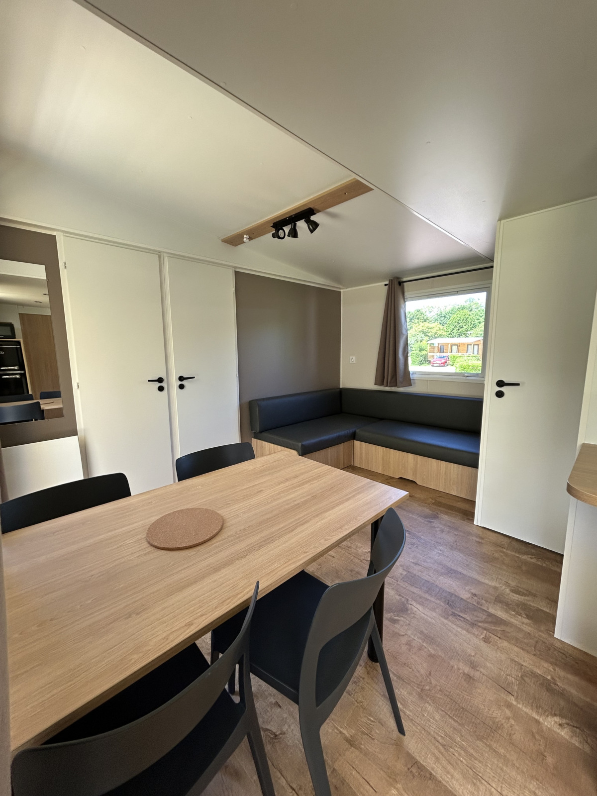 Interieur van een modern huisje met eettafel, zwarte stoelen en bank op Camping Seasonova Les Marguerites, Frankrijk.