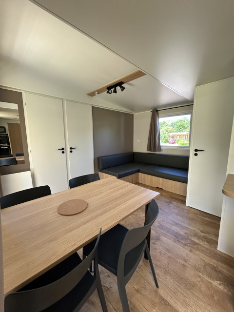 Interno di un cottage moderno con tavolo da pranzo, sedie nere e divano al Camping Seasonova Les Marguerites in Francia.