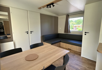 Innenraum einer modernen Hütte mit Esstisch, schwarzen Stühlen und Sofa auf Camping Seasonova Les Marguerites, Frankreich.