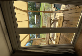 Vista a través de la ventana desde una cabaña en Camping Seasonova Les Marguerites en Francia, con terraza de madera.