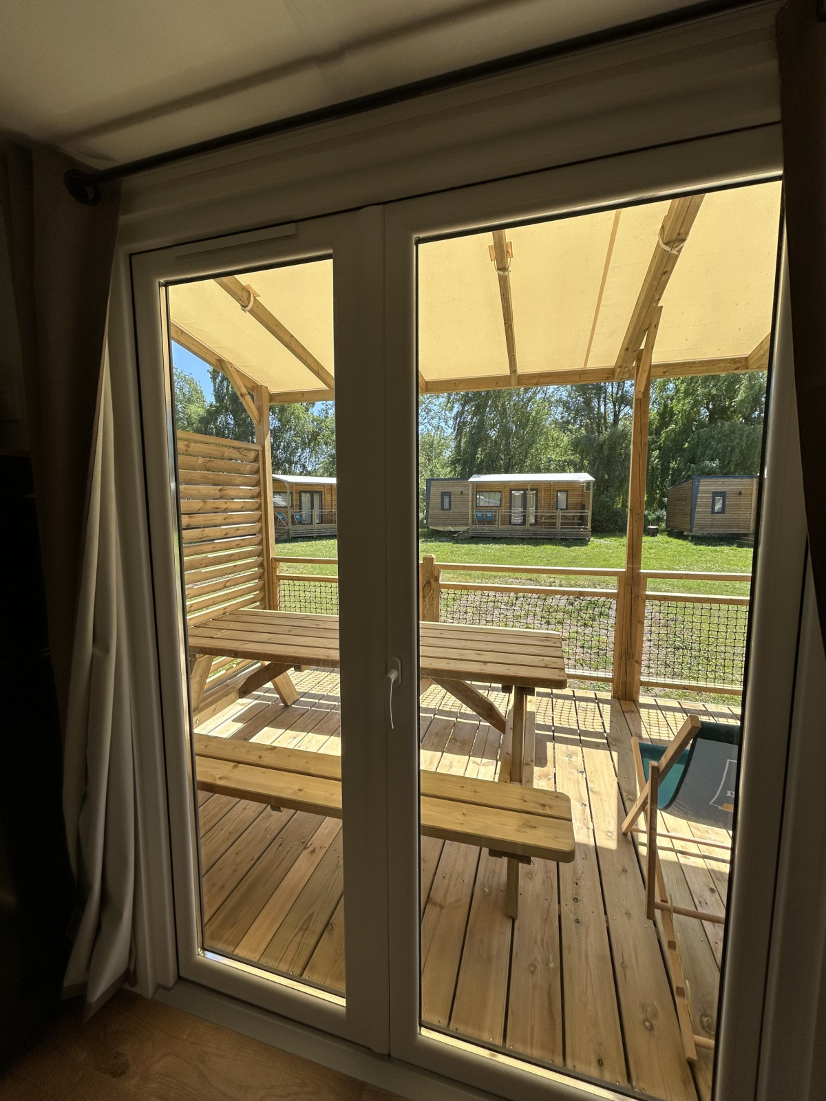 Uitzicht door het raam van een cottage op Camping Seasonova Les Marguerites in Frankrijk, houten terras buiten.