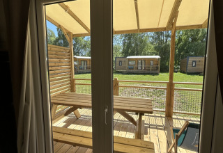 Vista a través de la ventana desde una cabaña en Camping Seasonova Les Marguerites en Francia, con terraza de madera.