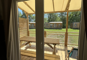 Foto taget gennem vindue fra en hytte hos Camping Seasonova Les Marguerites i Frankrig, udendørs træterrasse.
