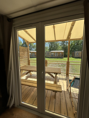 Vista a través de la ventana desde una cabaña en Camping Seasonova Les Marguerites en Francia, con terraza de madera.
