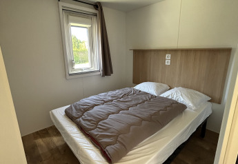 Schlafzimmer einer Cottage-Hütte im Camping Seasonova Les Marguerites in Frankreich mit Bett und Fenster.