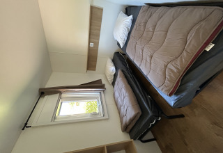 Vista interior de una cabaña en Camping Seasonova Les Marguerites con dos camas individuales, ventana y suelo de madera.