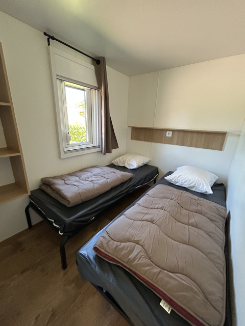 Vista interna di un cottage al Camping Seasonova Les Marguerites con due letti singoli, finestra e pavimento in legno.