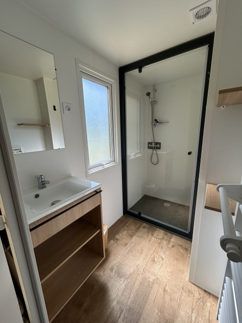 Baño moderno con ducha, piso imitación madera y lavabo en una cabaña de Camping Seasonova Les Marguerites, Francia.