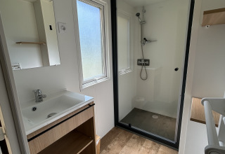 Baño moderno con ducha, piso imitación madera y lavabo en una cabaña de Camping Seasonova Les Marguerites, Francia.