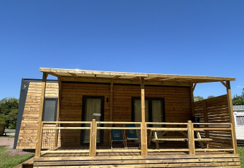Holzhütte am Camping Seasonova Les Marguerites in Frankreich mit Veranda, Rasen und blauem Himmel.