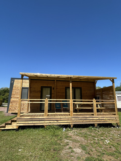 Holzhütte am Camping Seasonova Les Marguerites in Frankreich mit Veranda, Rasen und blauem Himmel.