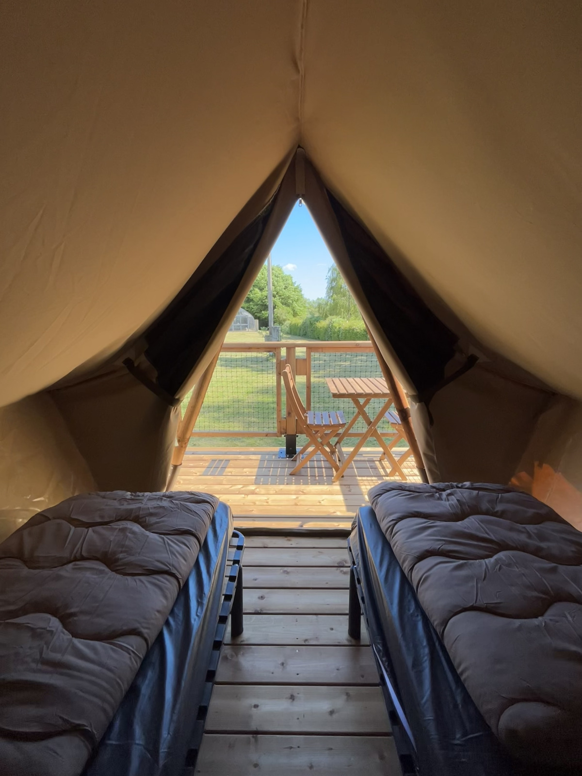 Binnenkant van een safaritent met twee bedden, uitzicht op een houten terras en groene natuur buiten.