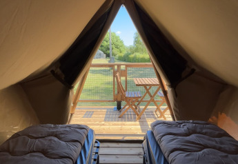 Inside a safari tent with two single beds, looking out onto a wooden deck and lush greenery outside.