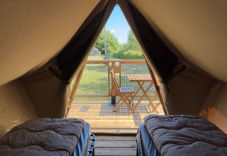 Binnenin een safaritent met twee bedden, zicht op een houten terras en groene omgeving buiten.