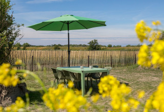 Buitenterras met groene tafel, stoelen en parasol in een landelijke omgeving bij Welcome In - Zeeland.