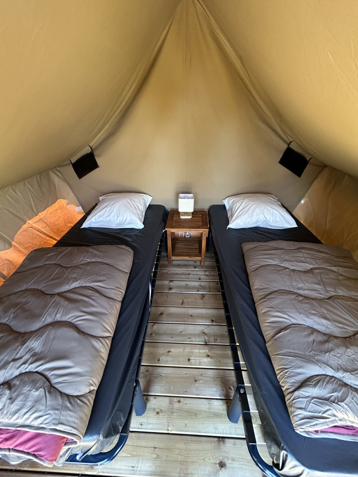 Interieur van het Nomads Bivoac safaritent met twee eenpersoonsbedden, nachtkastje en houten vloer bij Camping Seasonova Les Marguerites in Frankrijk.