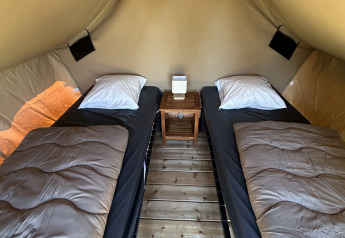 Vista interna della tenda safari Nomads Bivoac con due letti singoli, comodino e pavimento in legno al Camping Seasonova Les Marguerites in Francia.