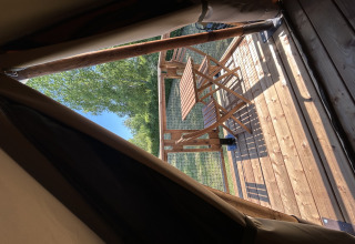Uitzicht vanuit een safaritent op een houten terras met tafel en stoelen bij Camping Seasonova Les Marguerites in Frankrijk.