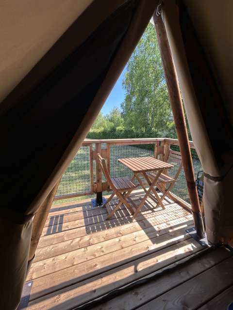 Vista dall'apertura di una tenda safari su una terrazza in legno con tavolo e sedie al Camping Seasonova Les Marguerites, Francia.