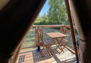 Vista dall'apertura di una tenda safari su una terrazza in legno con tavolo e sedie al Camping Seasonova Les Marguerites, Francia.