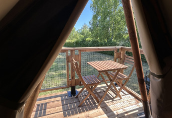 Vista dall'apertura di una tenda safari su una terrazza in legno con tavolo e sedie al Camping Seasonova Les Marguerites, Francia.