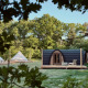 Et fredeligt naturområde med moderne hyttekabine og glampingtelte blandt frodige grønne træer.