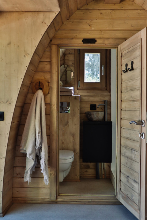 Badeværelse i en træhytte med håndklæde, toilet og lille vindue, set i Cabin at Thuysgrond, Holland.