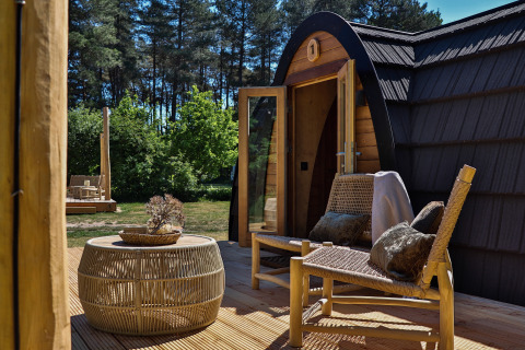Terrasse der Cabin at Thuysgrond in den Niederlanden mit geflochtenen Stühlen und Tisch, umgeben von Wald.