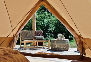 Zicht vanuit een Bell-tent tipi op Thuysgrond, Nederland, met zitbank en tafel op een houten terras.