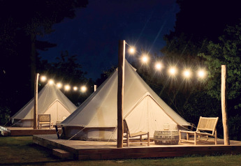 Bell-tenten bij nacht op Thuysgrond, Nederland, sfeervol verlicht met lichtslingers en tuinmeubels.