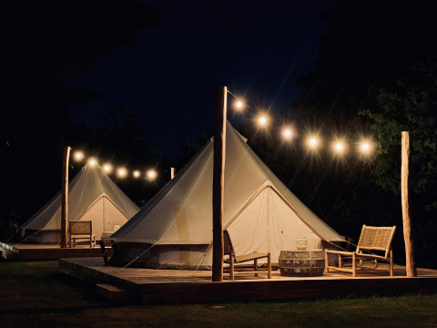 Tentes Bell éclairées la nuit à Thuysgrond, Pays-Bas, avec terrasse en bois, chaises et guirlande lumineuse.