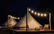 Bell tents at Thuysgrond, Netherlands at night, warmly lit with string lights and seating on wooden decks.