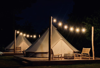 Bell tents at Thuysgrond, Netherlands at night, warmly lit with string lights and seating on wooden decks.