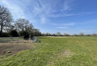 Sunny view of Feather Down Foxglove Farm holiday park in South East England with grassy fields and trees.