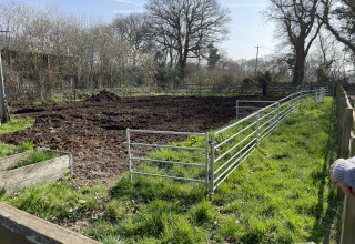 Fenced off dirt field at Feather Down Foxglove Farm holiday park, South East England, sunny day.