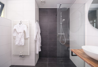 Bagno moderno in un lodge con doccia in vetro, lavabo tondo, piano in legno e due accappatoi bianchi.