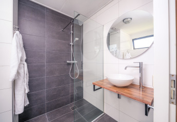 Modern bathroom at a lodge with large gray shower, wooden sink counter, round mirror and vessel sink.