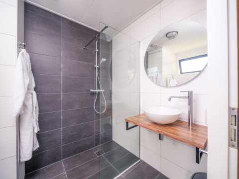 Modern bathroom at a lodge with large gray shower, wooden sink counter, round mirror and vessel sink.