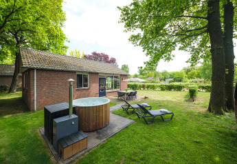 Outdoor view of FC Mölke lodge at Holiday Park Mölke, Netherlands, featuring hot tub, sun loungers and table.