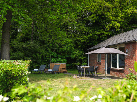 Cozy lodge at Holiday Park Mölke, Netherlands, featuring sun loungers, patio umbrella, and lush green forest.