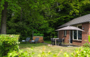Agradable lodge en Holiday Park Mölke, Países Bajos, con tumbonas, sombrilla y entorno de bosque verde.