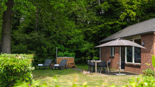 Knusse lodge bij Holiday Park Mölke, Nederland, met ligstoelen, parasol en omringd door groene natuur.