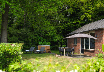 Cozy lodge at Holiday Park Mölke, Netherlands, featuring sun loungers, patio umbrella, and lush green forest.