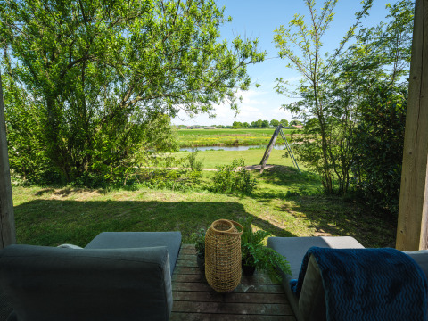 Blick von einer Lodge-Terrasse mit bequemen Sesseln, Garten, Fluss und einer Schaukel im Hintergrund.