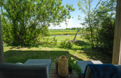 View from a lodge seating area with cozy chairs, green garden, river, and a swing set in the background.