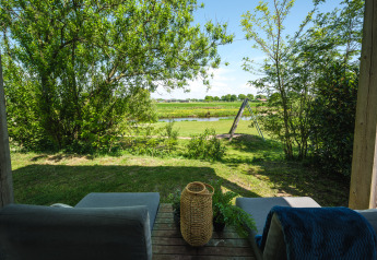 Vista desde una sala de descanso en una cabaña con sillones cómodos, jardín, río y columpio al fondo.