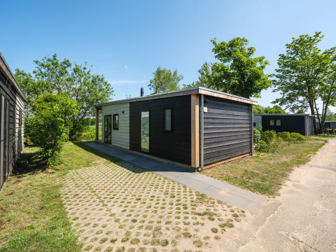 Moderne River Lodge ved Holiday Park Mölke i Holland, omgivet af grønne træer og blå himmel.