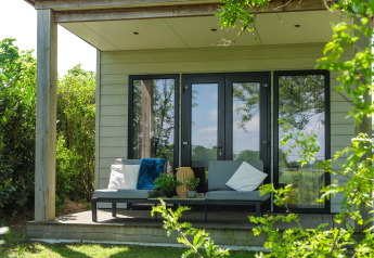 Cozy lodge porch with modern bench seating, soft pillows, decorative plants and lush greenery outside.