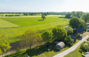 Vue aérienne d’une tiny house près d’une rivière et de champs verts au Holiday Park Mölke, Pays-Bas.